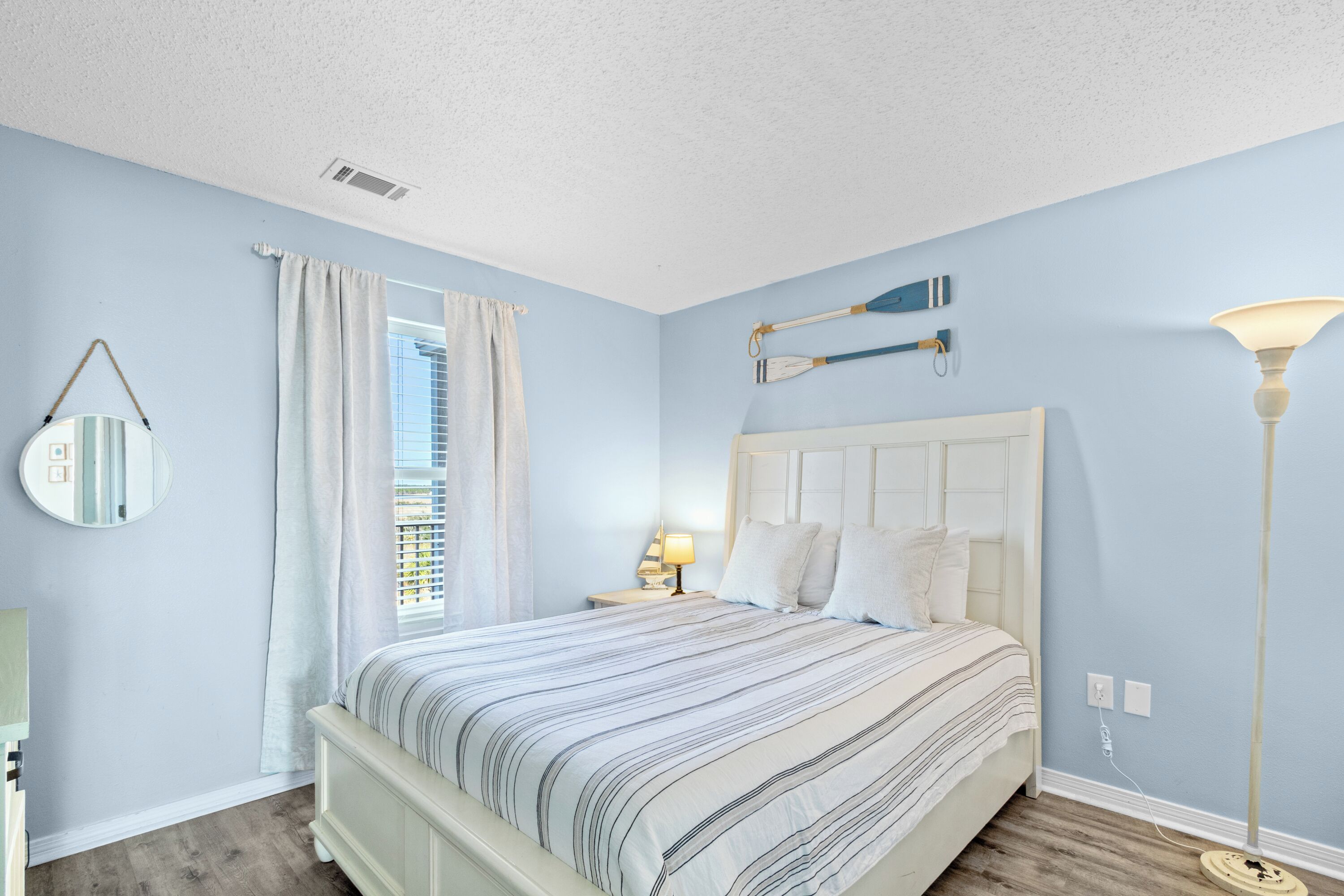 A bedroom with a bed, a nightstand, a lamp, a mirror, and a window with curtains.