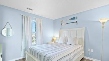 A bedroom with a bed, a nightstand, a lamp, a mirror, and a window with curtains.