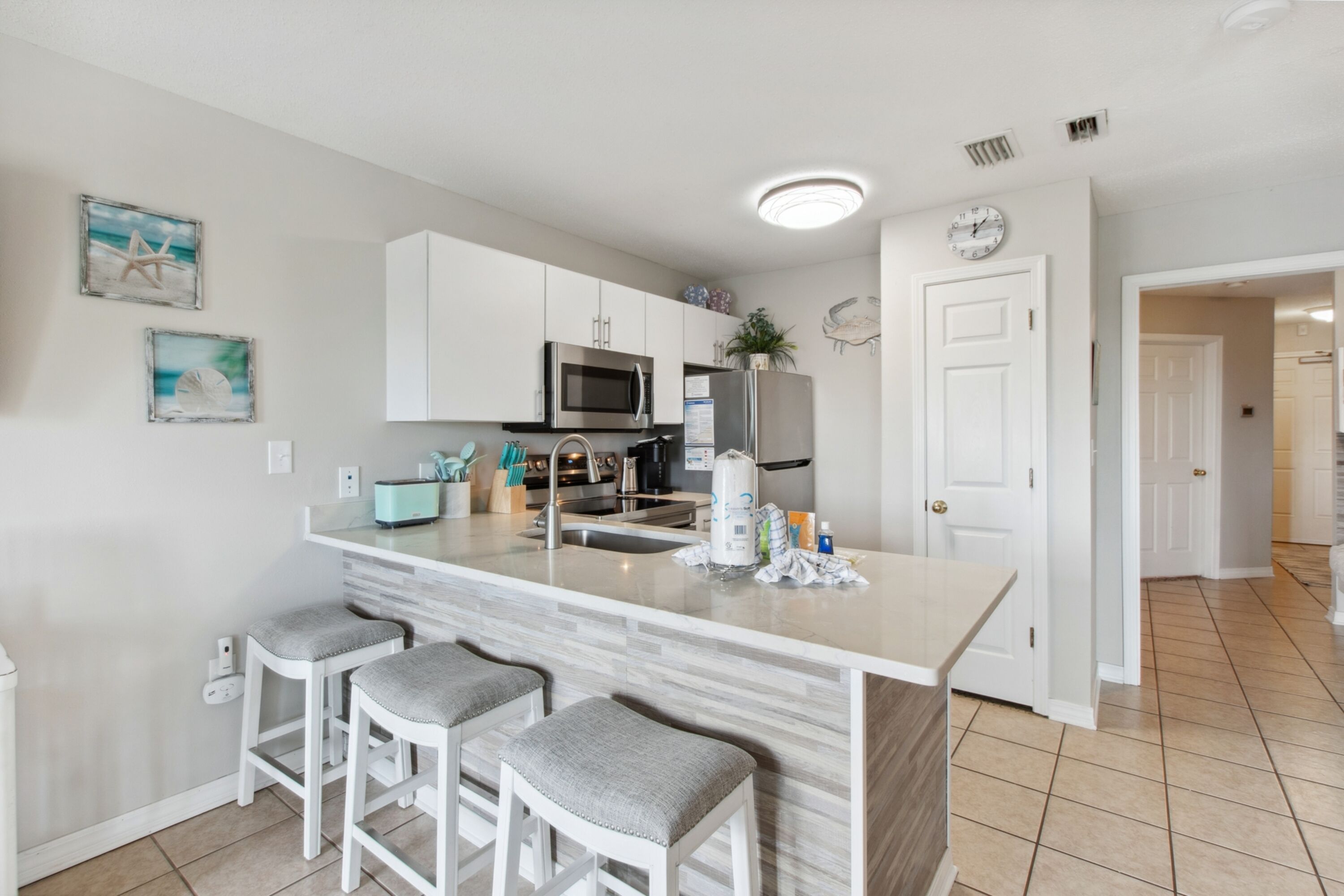 A modern kitchen with white cabinetry, a central island with bar stools, stainless steel appliances, and decorative wall art.
