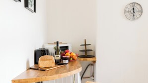 Una cucina con piano di lavoro in legno, tostapane, pane, bottiglia di vino, cestino di frutta e orologio a parete.