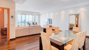 A modern living room with a glass dining table, beige sofas, wooden flooring, and a large window offering a view. - Puerto Banus Marina Apartment with Sea Views - Pass the Keys (Puerto  Banus)
