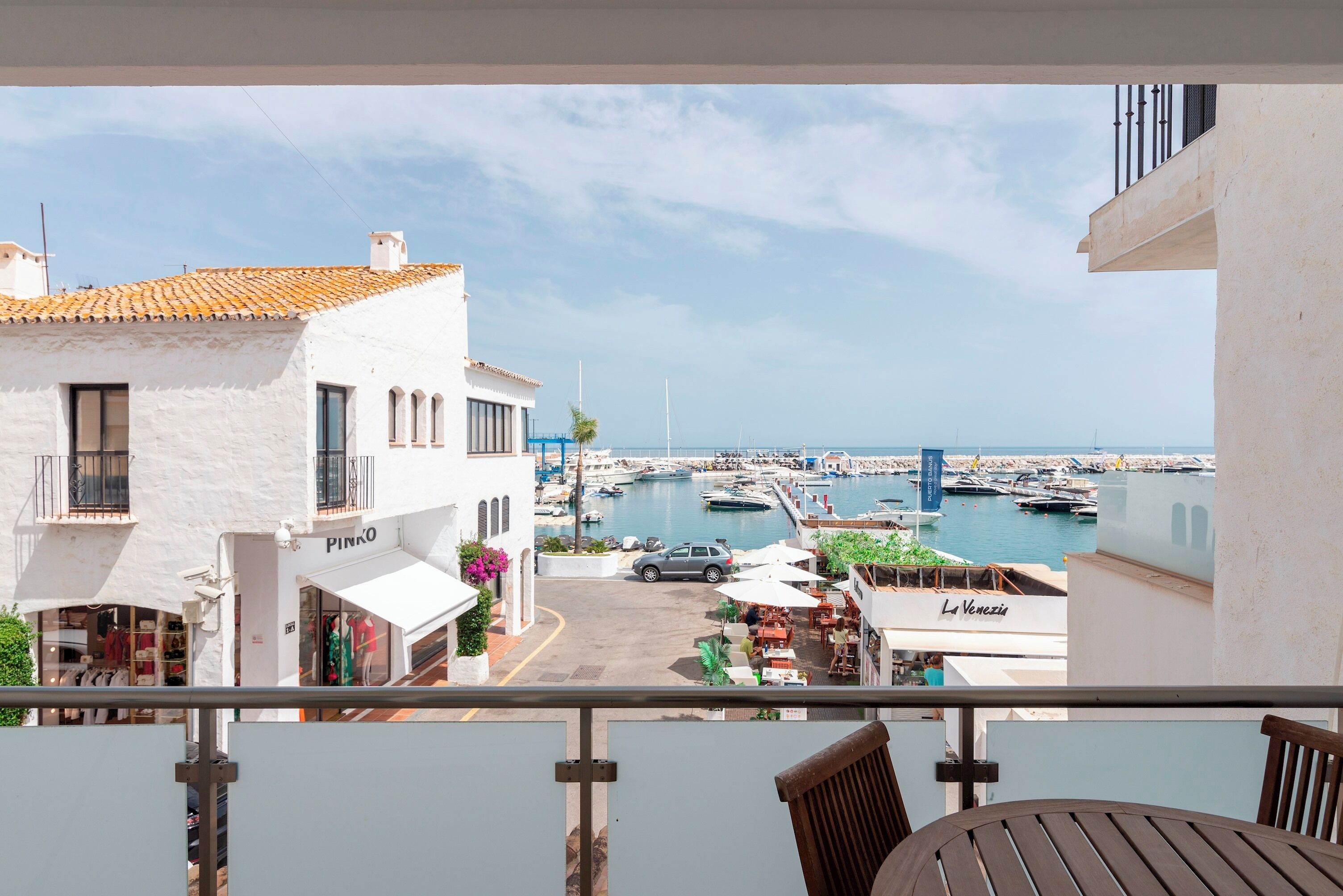 A balcony with a view of a marina, a white building with a shop named 'PINKO', and a restaurant named 'La Venezia'.