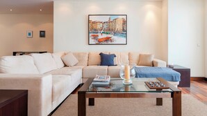A modern living room with a beige sofa, a glass coffee table, and a framed painting of a coastal scene. - Puerto Banus Marina Apartment with Sea Views - Pass the Keys (Puerto  Banus)
