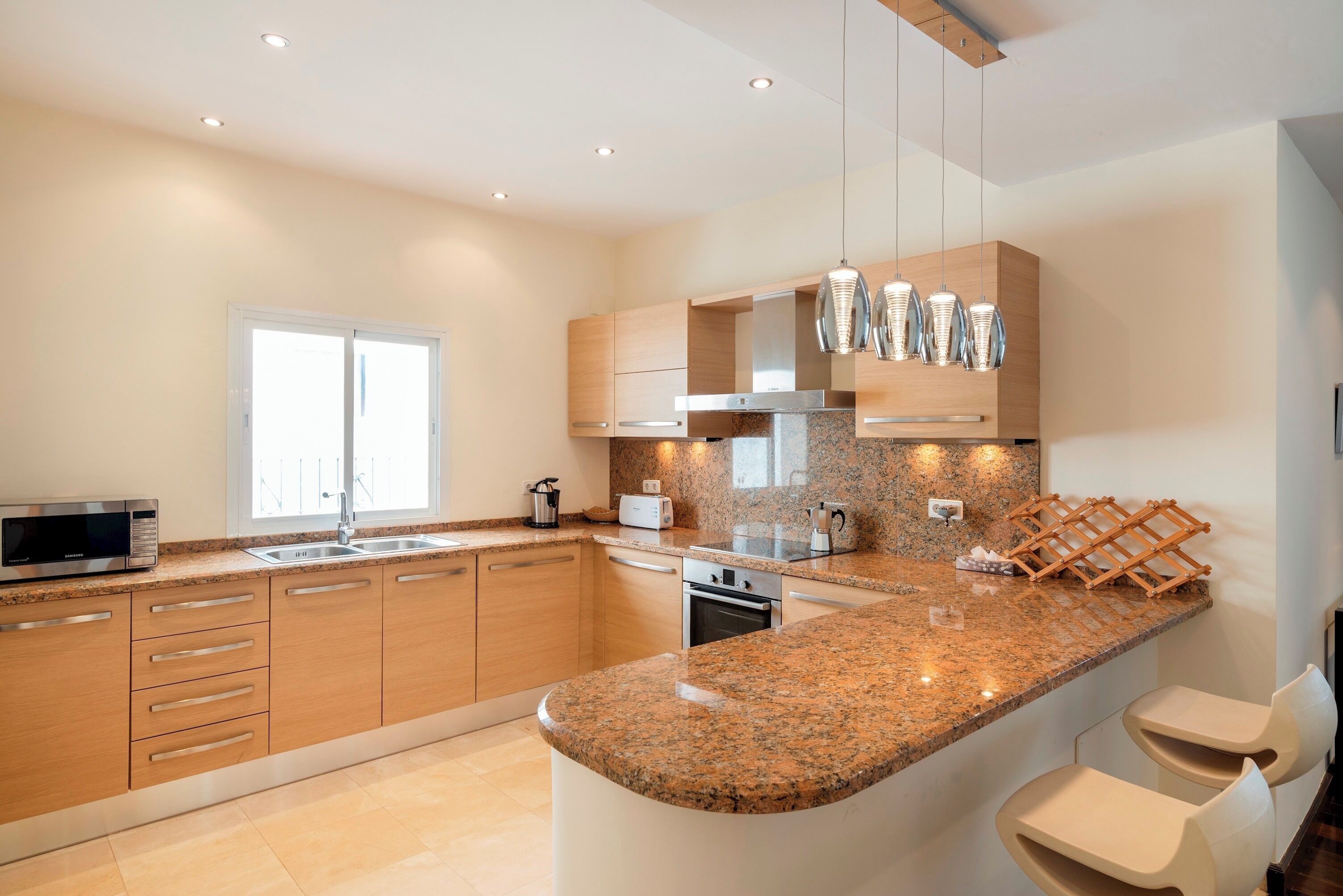 Eine moderne Küche mit Granit Arbeitsplatten, Edelstahlgeräten, Holzschränken und Pendelleuchten.