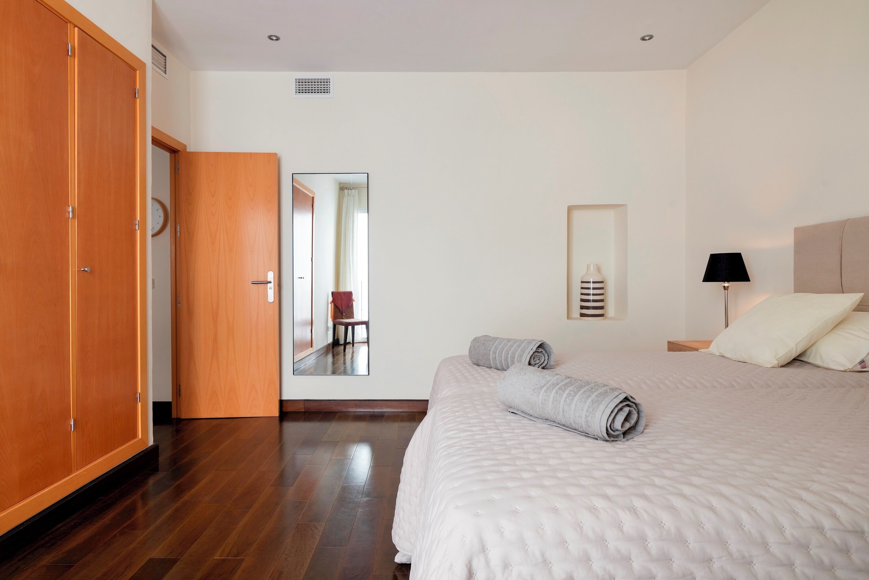 Ein Hotelzimmer mit einem großen Bett, einem Holzschrank, einem Spiegel und einem Nachttisch mit einer Lampe.