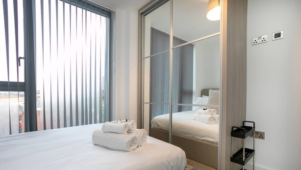 Moderni hotellihuone, jossa on suuri sänky, peili ja ikkunasta avautuva näkymä kaupunkiin.