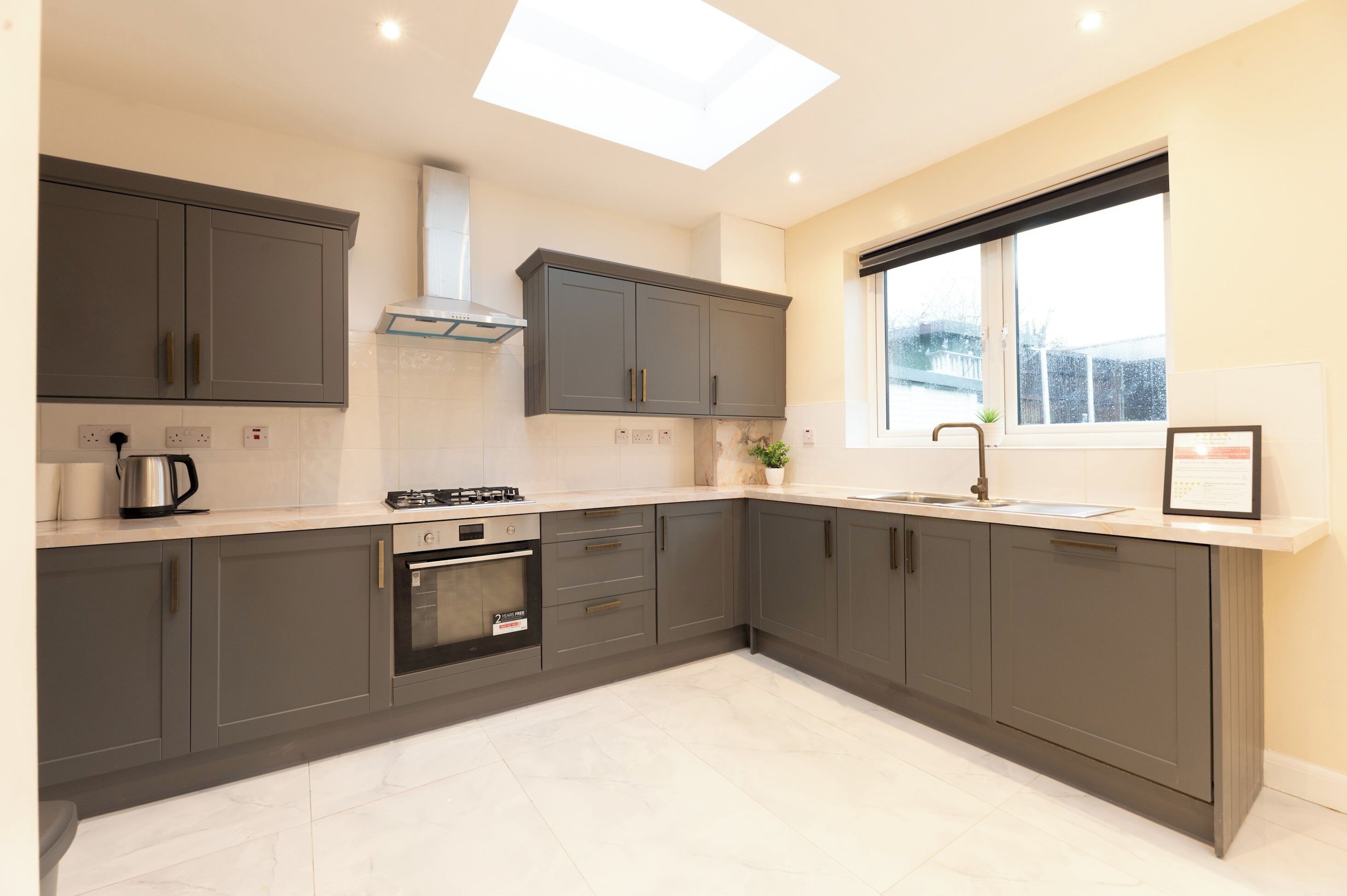 A modern kitchen with grey cabinets, a gas stove, an oven, and a skylight.
