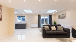 Ein modernes Wohnzimmer mit einem dunkelgrauen Sofa, einem Couchtisch und Blick auf die Küche und den Essbereich durch eine Glastür.