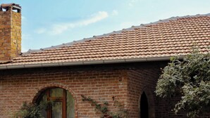 A brick house with a tiled roof, a small arched window, and a staircase leading to the entrance. - Kuzey Dunna Barba (Avanos)