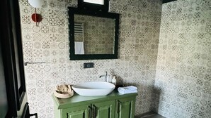 Un baño con paredes con diseño, un tocador verde, dos lavamanos, un espejo y una ventana.