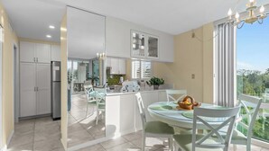 Una cucina moderna con mobili bianchi, un frigorifero e un'area pranzo con tavolo e sedie in vetro.