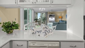 Una cucina con mobili bianchi, lavastoviglie e zona pranzo con tavolo e sedie.