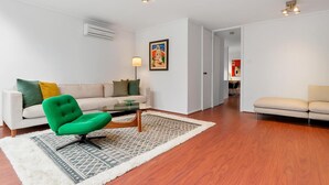 En moderne stue med en grøn lænestol, en beige sofa og et mønstret tæppe.