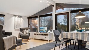 A modern dining area with a table set for four, surrounded by chairs. There is a large window providing a view of the outdoors. - "Ordan" - 140m to the fjord by Interhome (Jægerspris)