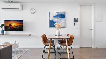 A modern dining area with a wooden table, four chairs, a vase, and a painting on the wall.