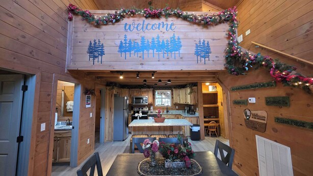 Interior de una cabaña de madera con un cartel que dice 'welcome', un comedor, cocina y un letrero que indica 'Green Mountain National Park 10 km'.