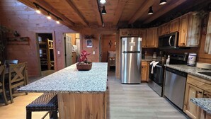 Una cocina con gabinetes de madera, encimeras de granito y electrodomésticos de acero inoxidable, incluyendo un refrigerador y un microondas.