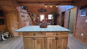 Interior de una cabaña de madera con una isla de cocina de granito, armarios de madera y un comedor con mesa y sillas.