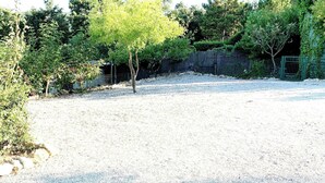 Un aparcamiento de grava con árboles y una valla al fondo.