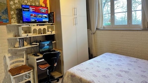 Un dormitorio con una cama, un escritorio con computadora, un televisor y un armario.