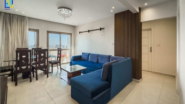 Un salon moderne avec un canapé bleu, une table à manger avec des chaises et un lustre.