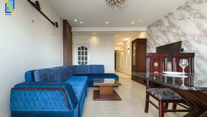 Un salon moderne avec un canapé d’angle bleu, une table basse en verre et un coin repas agrémenté d’un mur en marbre et de meubles en bois.