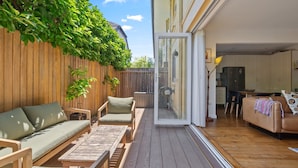A spacious patio with a wooden deck, a sofa, a dining table, and a sliding glass door leading to an indoor area with a kitchen and a seating area. - Spacious Stay Near Shops & Cafes in Marrickville (Sydney)