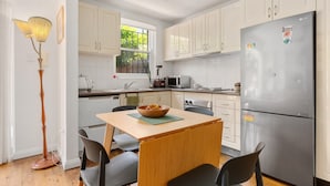 A modern kitchen with white cabinets, a stainless steel refrigerator, a dining table with chairs, and a floor lamp. - Spacious Stay Near Shops & Cafes in Marrickville (Sydney)