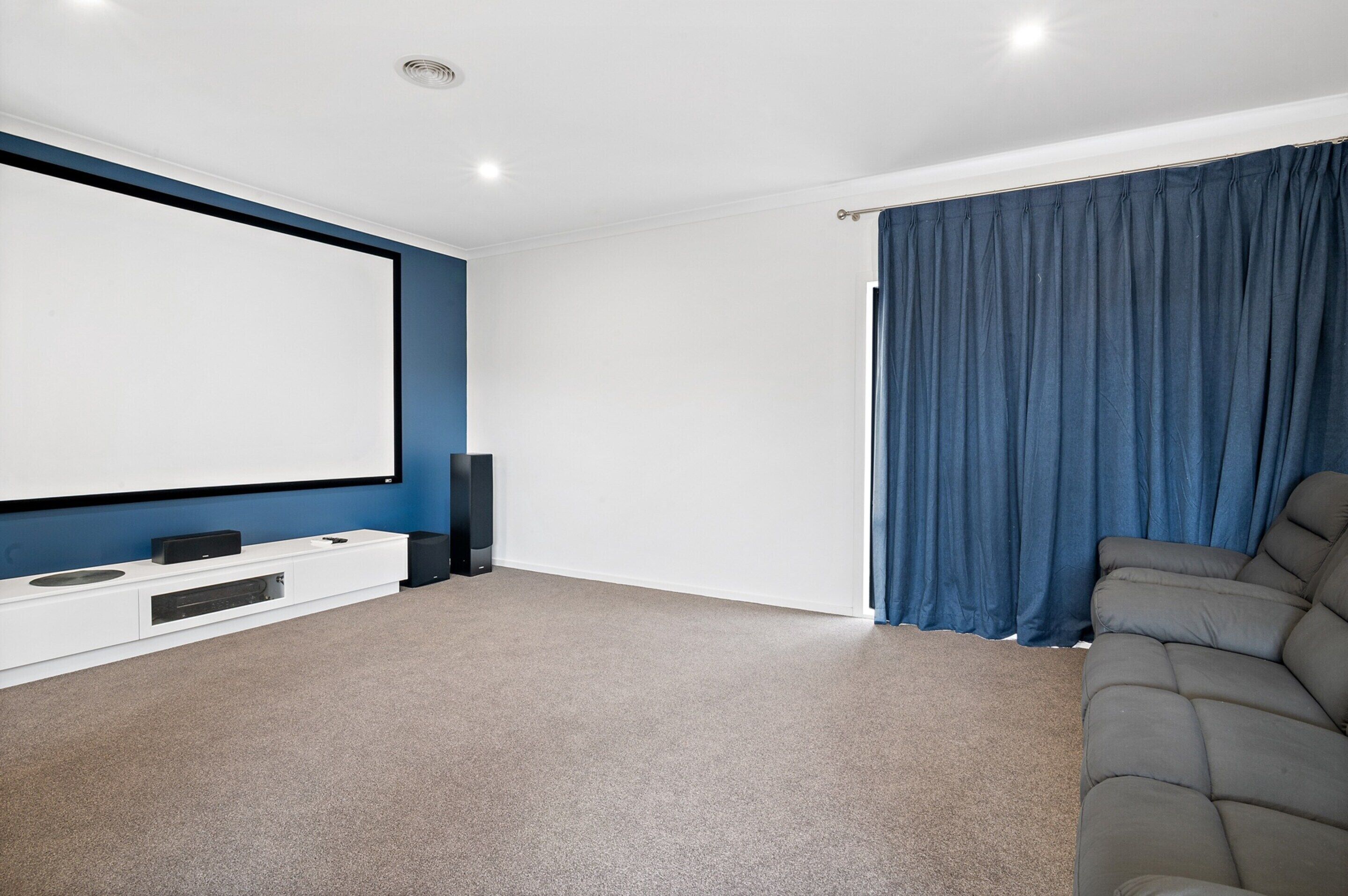 Un salon moderne doté d’un grand téléviseur à écran plat, d’un canapé confortable de couleur grise et d’un rideau bleu foncé.