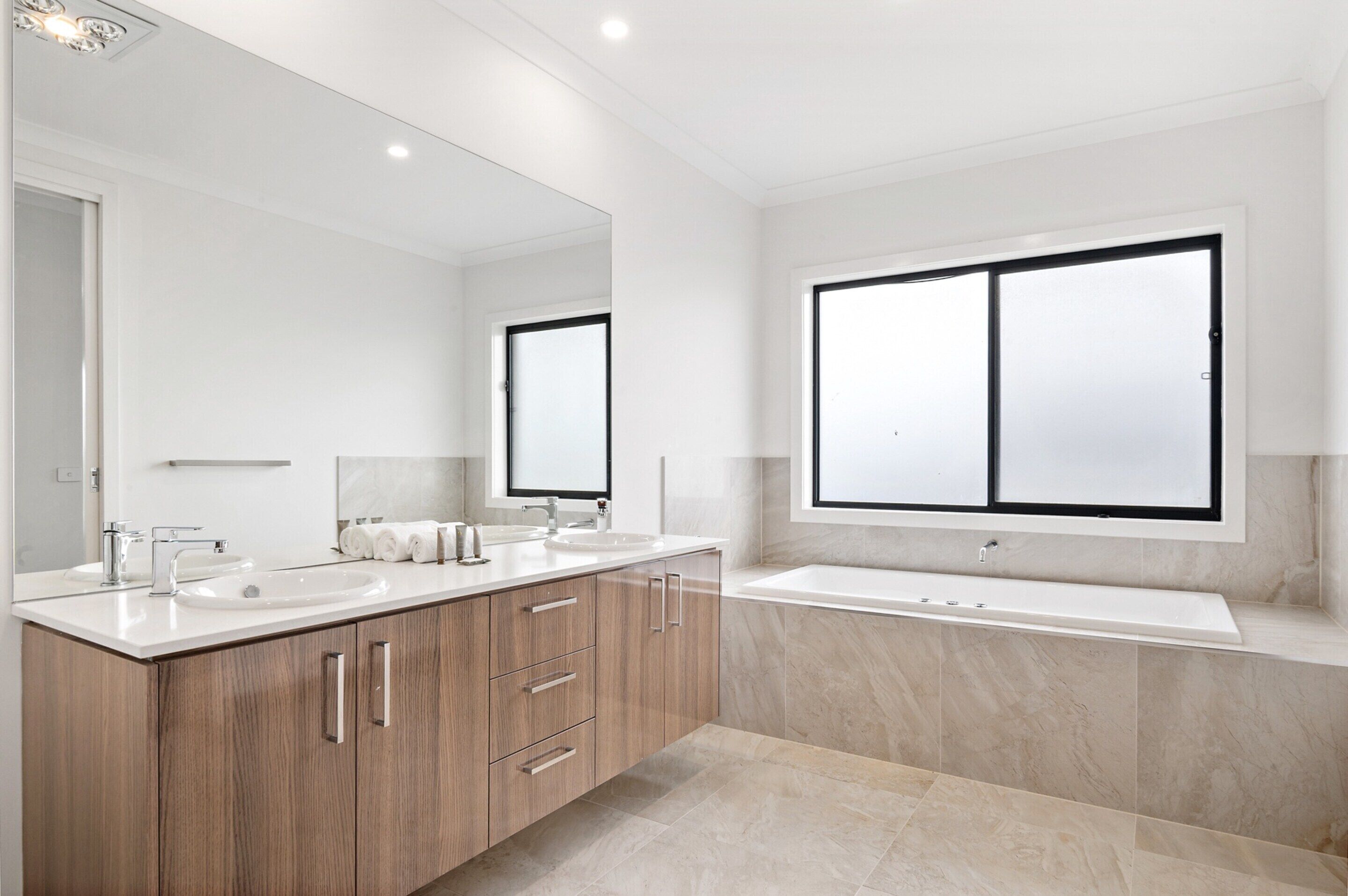 A modern bathroom with two sinks, a large mirror, and a bathtub.