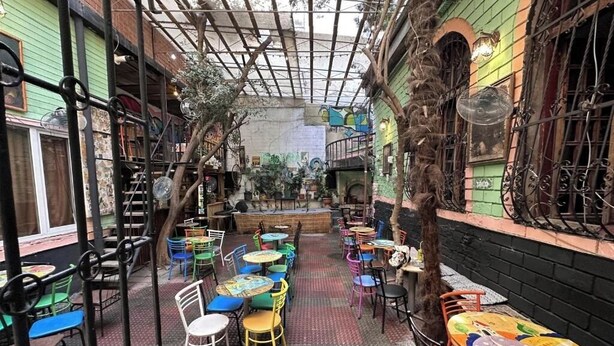 An outdoor café with tables and chairs, surrounded by brick walls and greenery. - Flora Hostel Baku (Baku)