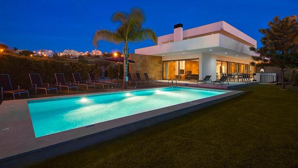 Ein modernes Haus mit Swimmingpool, Liegestühlen und einem gepflegten Rasen.