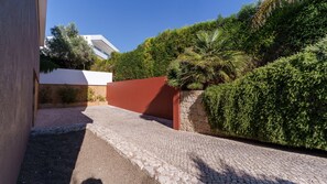 A paved pathway leading to a building with a red wall and a stone wall with greenery. - Villa Marina Casa Luxuosa c/Piscina by LovelyStay (Ferragudo)