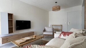 Ett modernt vardagsrum med en soffgrupp, ett soffbord, en tv som är monterad på väggen och en hängande lampa.