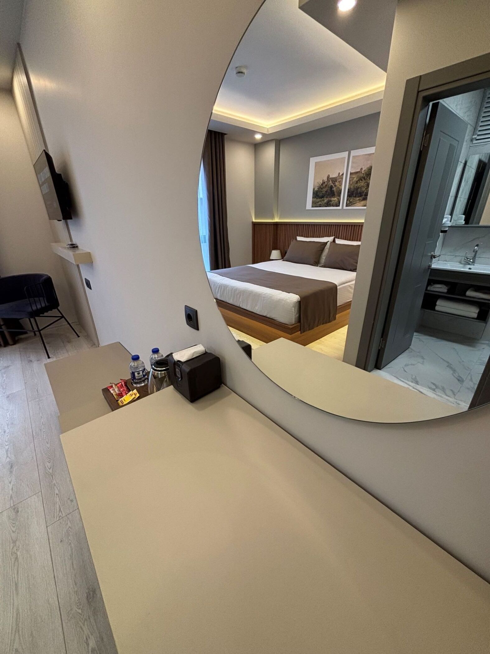 Une chambre d’hôtel moderne, équipée d’un lit, d’une table de chevet et d’un grand miroir qui reflète la pièce.