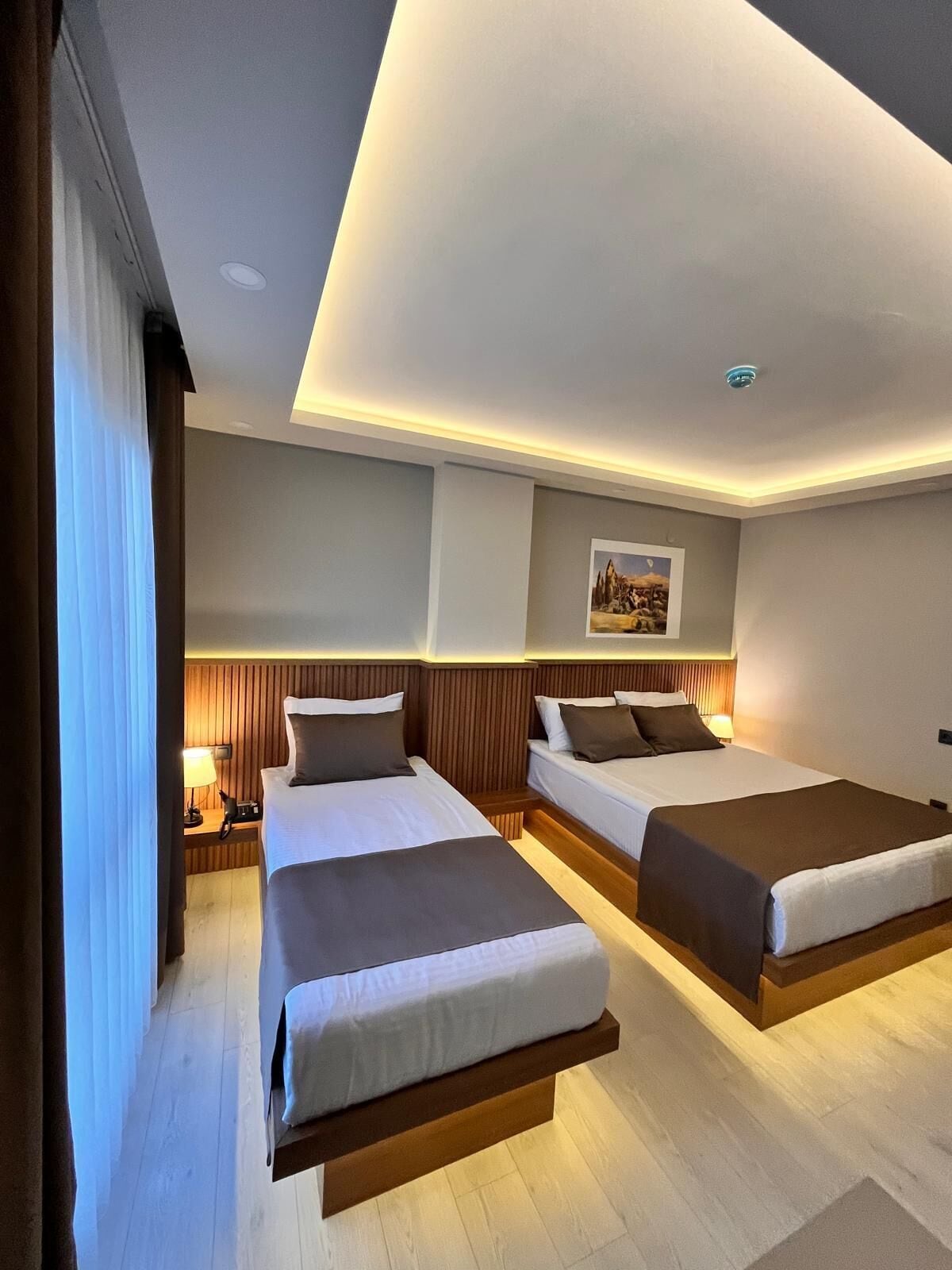 A hotel room with two beds, wooden headboards, a painting on the wall, and a nightstand with a lamp.