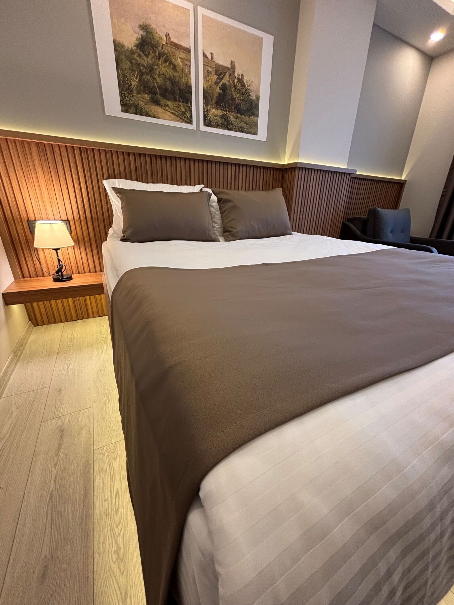 Una habitación de hotel moderna con una cama grande, cabecero de madera y una mesita de noche con lámpara.