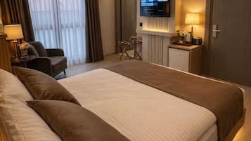 A hotel room with a large bed, a desk with a lamp, a television, and a wardrobe.
