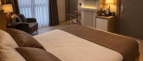 A hotel room with a large bed, a desk with a lamp, a television, and a wardrobe.