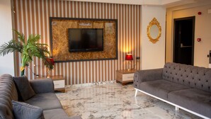 Una sala de estar moderna con un televisor de pantalla plana montado en una pared de mármol, un sofá gris, una lámpara roja y un espejo decorativo.