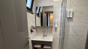 Un baño con piso de mármol, un lavamanos con espejo y una cabina de ducha de vidrio, además de un perchero para toallas.