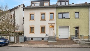 A row of townhouses with a garage on the right, a small front yard, and a clear sky. - Cozy in the old town and nature (Trier)