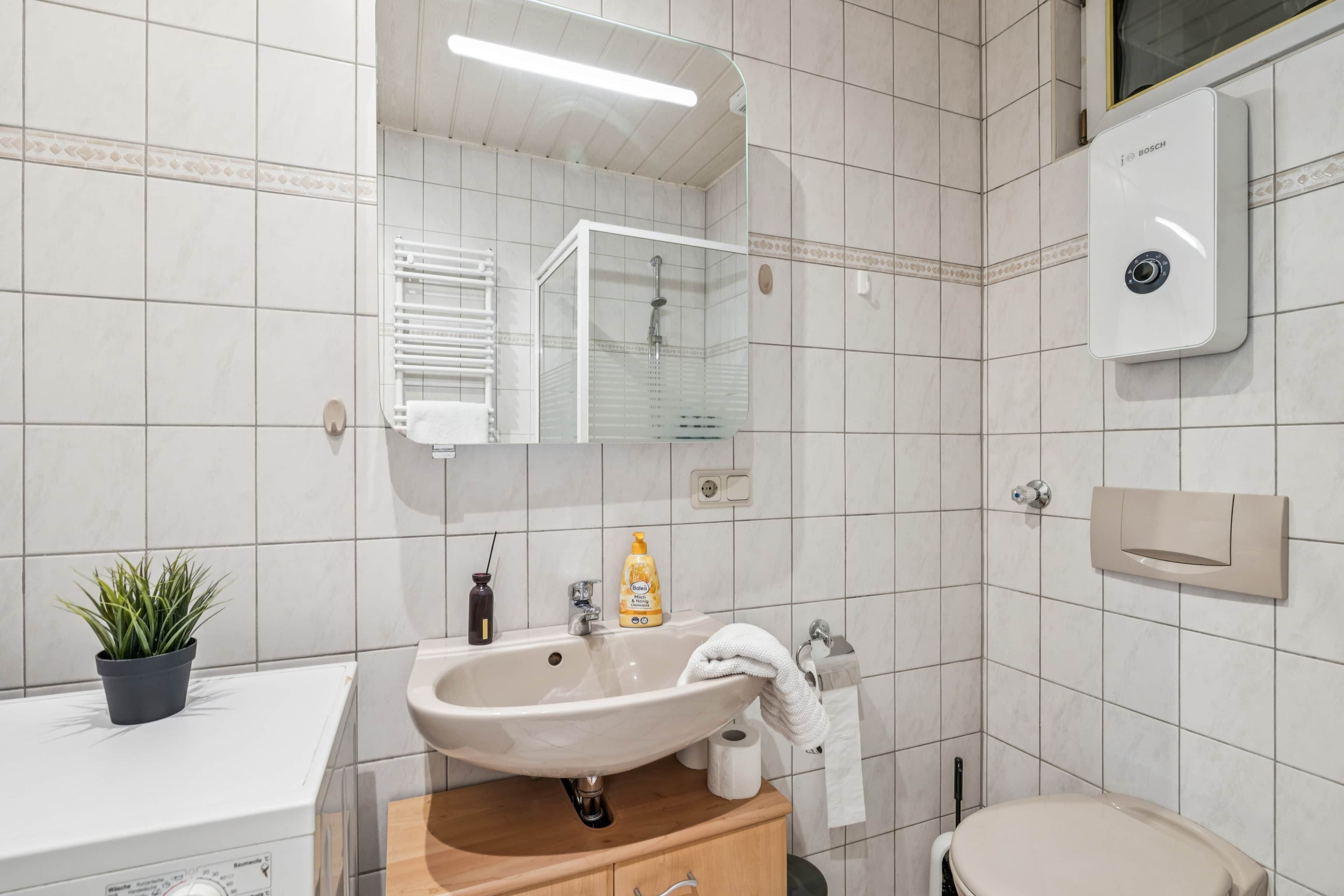Une salle de bain équipée d’un lavabo, d’un miroir, de toilettes et d’un chauffe-eau Bosch.