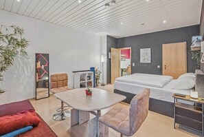 A modern hotel room with a bed, a desk, a chair, a sofa, a small table, and a mirror. - Cozy in the old town and nature (Trier)