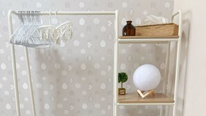 Une étagère en métal blanc, avec un panier tressé, un panier blanc perforé et une petite plante posée sur une étagère.
