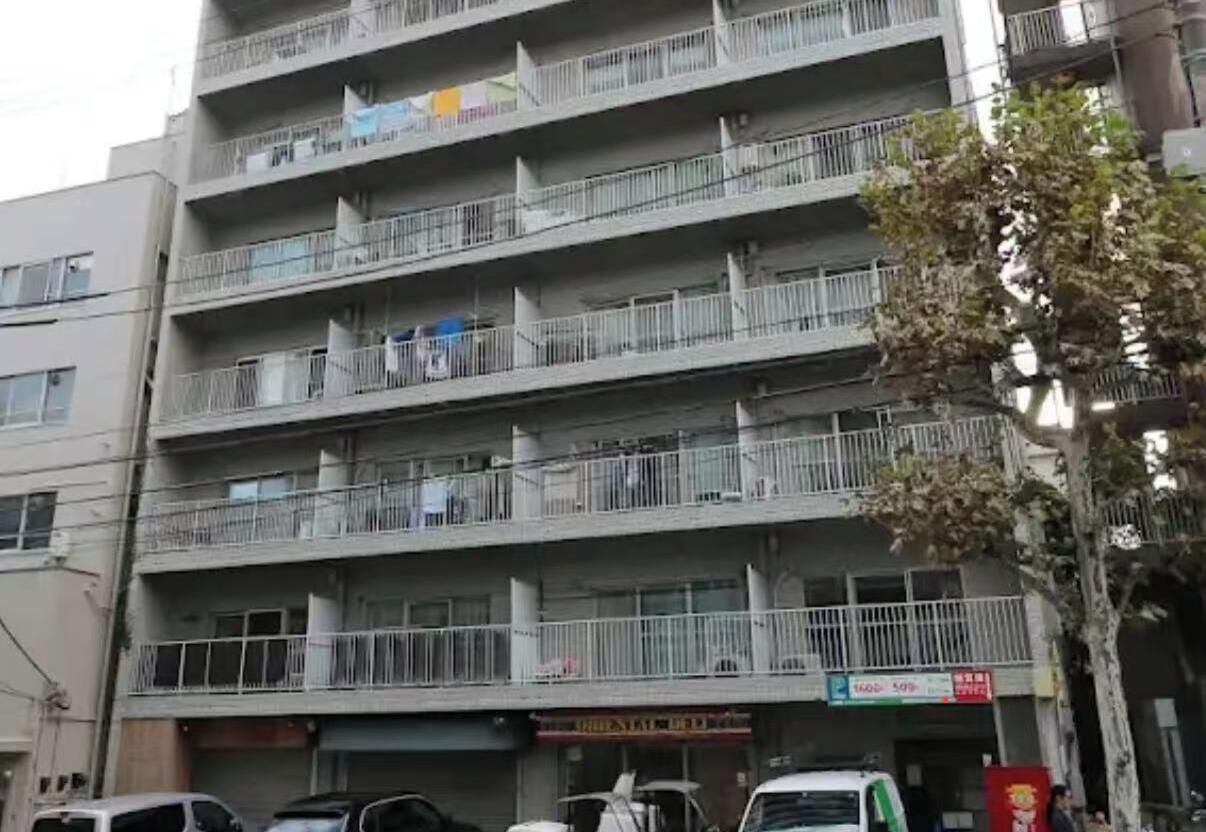 Ein mehrstöckiges Gebäude mit Balkonen, einer sichtbaren Schaufensterfront und parkenden Autos.