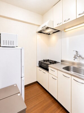 A compact kitchen with white cabinets, a stainless steel sink, a gas stove, and a microwave on top of a white refrigerator. - Minato-ku, Tokyo tourism, direct access to the airport, 2K, room with a view of Tokyo Tower (東京都港区高輪1−5−19)