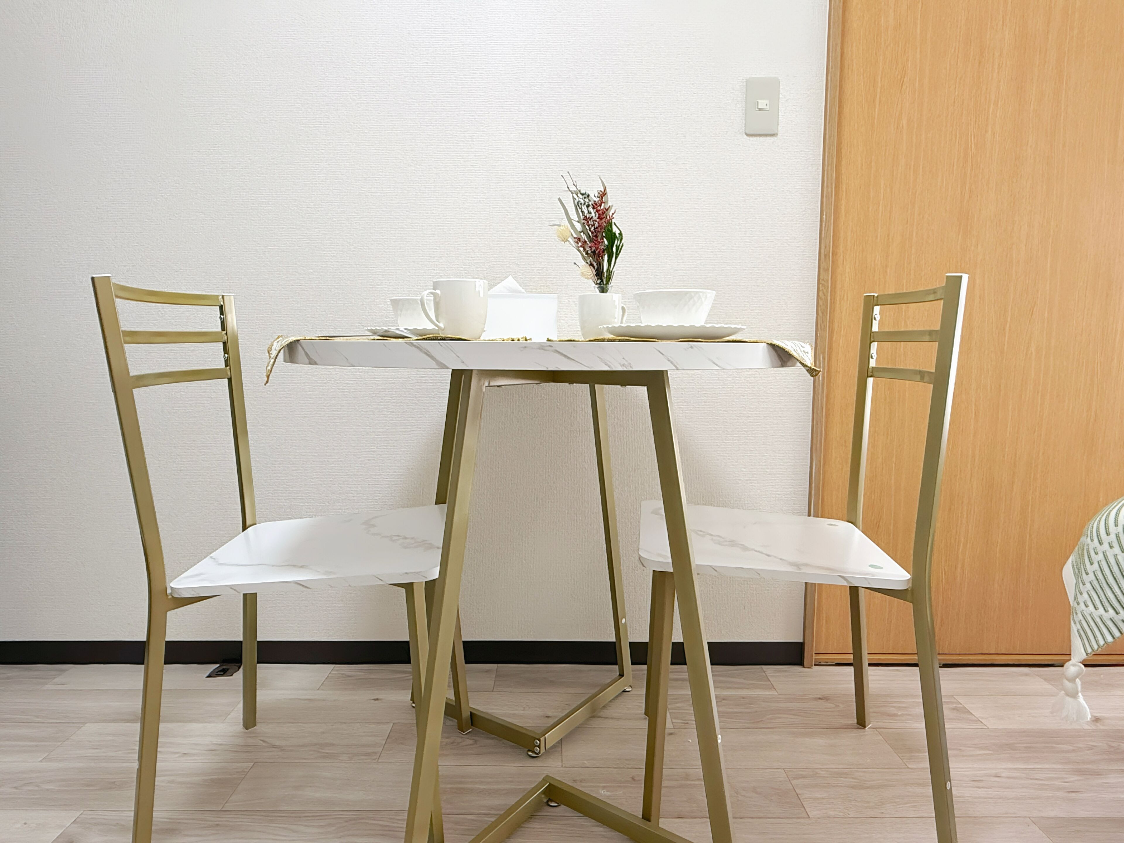 A dining area with a white table and chairs, a small vase with flowers, and a wooden door.