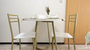 Un coin repas avec une table et des chaises blanches, un petit vase avec des fleurs et une porte en bois.