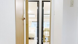 Un couloir menant à une chambre à coucher qui contient un lit, une chaise et une fenêtre.